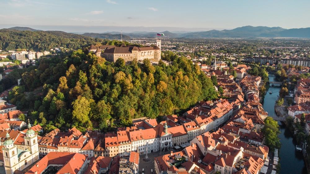 Lublaňský hrad na kopci nad městem, obklopený lesem a s výhledem na střechy centra.